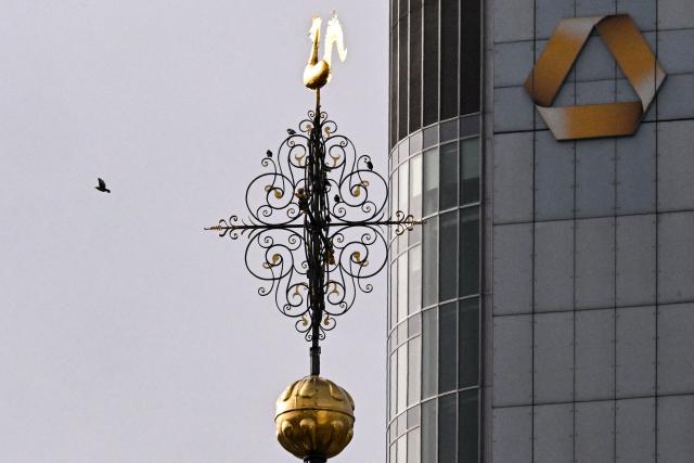 A bird flies past the weathercock atop the Evangelical Lutheran St. Catherine's Church, with the Commerzbank logo on the bank's headquarters building in the background, in the banking district of Frankfurt am Main, western Germany, on October 26, 2026. (Photo by Kirill KUDRYAVTSEV / AFP)