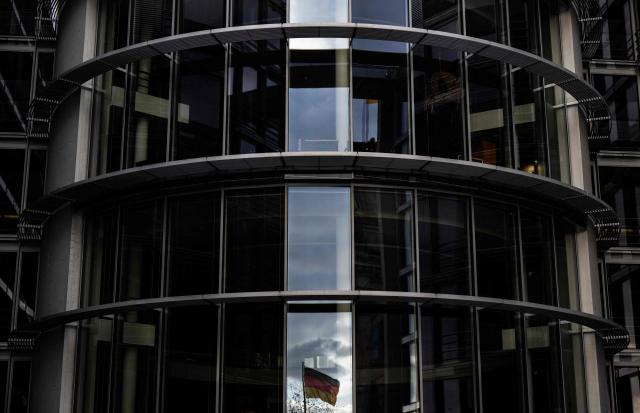 The German flag flying in front of the Reichstag building is reflected in the window of the Paul-Loebe-Haus parliamentary complex in Berlin on October 26, 2026. (Photo by John MACDOUGALL / AFP)