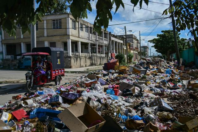 A tricycle rickshaw passes by piles of uncollected garbage on a street in Havana, Cuba, on October 26, 2026. (Photo by YAMIL LAGE / AFP)