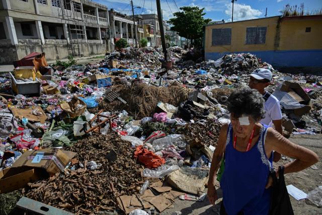 People walk past piles of uncollected garbage on a street in Havana, Cuba, on October 26, 2026. (Photo by YAMIL LAGE / AFP)
