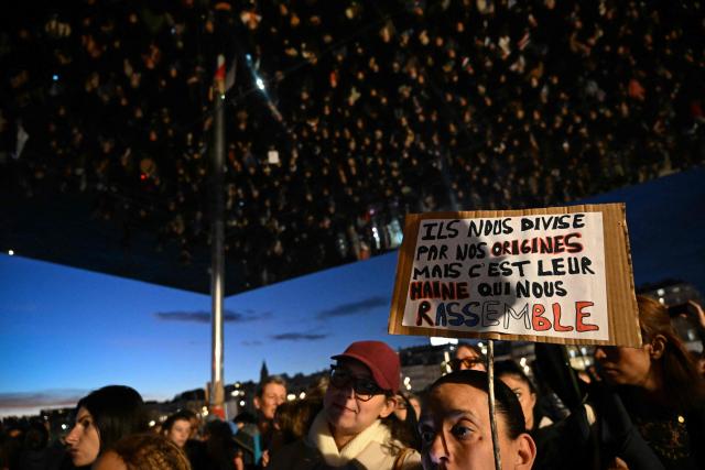 A woman holds a placard which reads "They divide us by our origins but it is their hatred that unites us" during a tribute to the victims of the Trappes attacks, in Marseille, on October 26, 2026. A man suspected of a gun attack in the Paris suburbs that killed Pengo Bossio Wangi and wounded five other persons has left custody and been placed in a psychiatric unit for observation, French anti-terror prosecutors said on October 25, 2026. The 39-year-old suspect, partly identified as Kevin T., was arrested on October 23, in possession of a submachine gun and tear-gas grenades in his car, shortly after the victims were shot as a vehicle drove through the working-class town of Trappes and neighbouring La Verriere. (Photo by Justine MEDDAH / AFP)