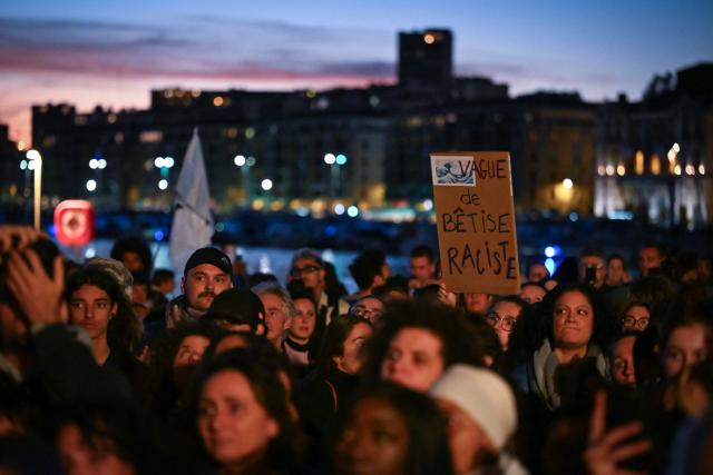 A person holds a placard that reads "Wave of Rascist stupidity" during a tribute to the victims of the Trappes attacks, in the Old Port in Marseille, on October 26, 2026. A man suspected of a gun attack in the Paris suburbs that killed Pengo Bossio Wangi and wounded five other persons has left custody and been placed in a psychiatric unit for observation, French anti-terror prosecutors said on October 25, 2026. The 39-year-old suspect, partly identified as Kevin T., was arrested on October 23, in possession of a submachine gun and tear-gas grenades in his car, shortly after the victims were shot as a vehicle drove through the working-class town of Trappes and neighbouring La Verriere. (Photo by Justine MEDDAH / AFP)