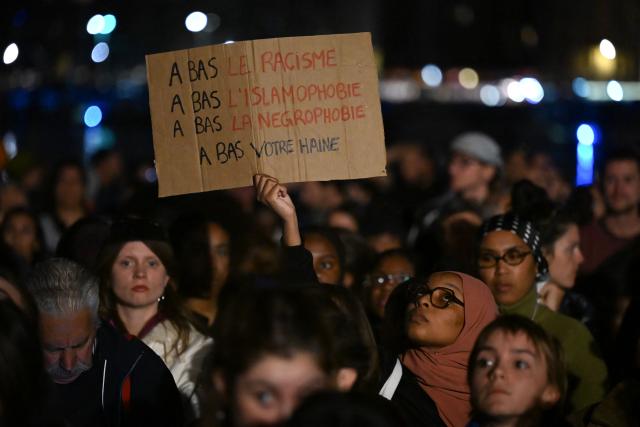 A person holds a placard which reads "Down with Racism, Down with Islamophobia, Down with Negrophobia, Down with your hate" during a tribute to the victims of the Trappes attacks, in the Old Port in Marseille, on October 26, 2026. A man suspected of a gun attack in the Paris suburbs that killed Pengo Bossio Wangi and wounded five other persons has left custody and been placed in a psychiatric unit for observation, French anti-terror prosecutors said on October 25, 2026. The 39-year-old suspect, partly identified as Kevin T., was arrested on October 23, in possession of a submachine gun and tear-gas grenades in his car, shortly after the victims were shot as a vehicle drove through the working-class town of Trappes and neighbouring La Verriere. (Photo by Justine MEDDAH / AFP)