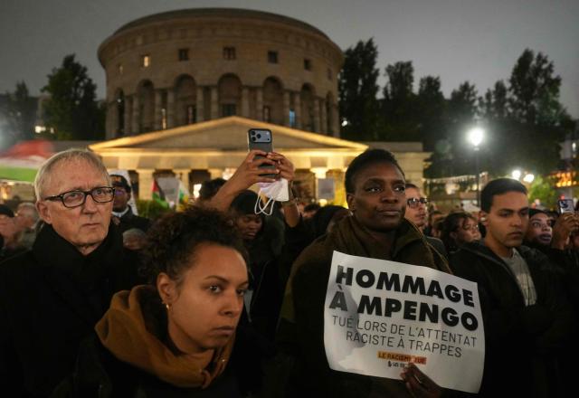 A protester holds a placard reading "tribute to M.Pengo killed during the racist terror attack in Trappes" with Rotonde Stalingrad building in the background during a gathering organised by SOS Racisme and other anti-racism organisations at Place de la Bataille-de-Stalingrad in Paris, on October 26, 2026, to denounce the normalisation of racist hatred and pay tribute to the victims of October 23 deadly shooting in Trappes in the Yvelines region. Marches were held on October 25 in tribute to a man killed in the shooting, Pengo Bossio Wangi, a 26-year-old French national of Congolese origin, and more were planned for today in several French cities, including Paris. (Photo by Dimitar DILKOFF / AFP)