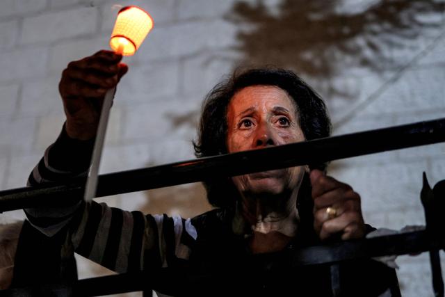 A woman stands with a candle during a vigil at the Greek Orthodox Church of the Transfiguration in the Palestinian city of Ramallah in the Israeli-occupied West Bank, on October 26, 2026, in solidarity with the victims of an attack on the Church of St George in Jordan's village of Hammoud on October 23. On October 23, gunmen stormed the compound of the Greek Orthodox St George's Church in the village of Hammoud in Karak governorate during a funeral procession, killing nine. Karak is home to a significant Christian community in Muslim-majority Jordan, where Christians make up between two and three percent of the population. (Photo by Zain JAAFAR / AFP)