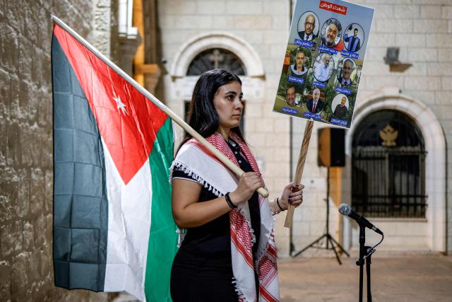 A mourner holds a Jordanian flag and a sign depicting the victims of an attack on the Church of St George in Jordan's village of Hammoud on October 23, during a memorial vigil at the Greek Orthodox Church of the Transfiguration in the Palestinian city of Ramallah in the Israeli-occupied West Bank, on October 26, 2026. On October 23, gunmen stormed the compound of the Greek Orthodox St George's Church in the village of Hammoud in Karak governorate during a funeral procession, killing nine. Karak is home to a significant Christian community in Muslim-majority Jordan, where Christians make up between two and three percent of the population. (Photo by Zain JAAFAR / AFP)