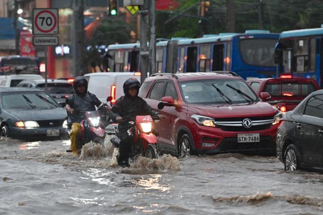 Motorcycles and cars make their way through flooded waters after heavy rains in north of Guayaquil, Ecuador on October 26, 2026. (Photo by MARCOS PIN / AFP)
