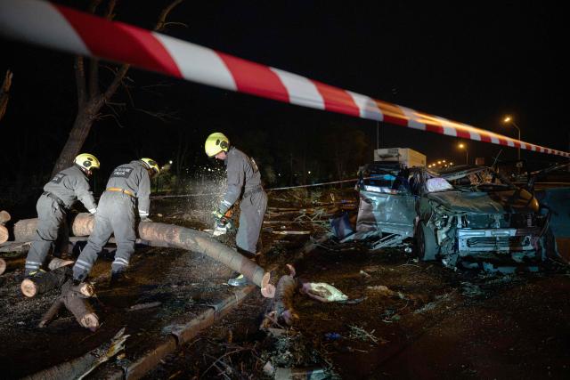 Ukrainian rescuers clear fallen trees near a destroyed car on a road in Kyiv on October 27, 2026, following a Russian missile strike. (Photo by Genya SAVILOV / AFP)