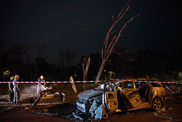 Ukrainian rescuers clear fallen trees near a destroyed car on a road in Kyiv on October 27, 2026, following a Russian missile strike. (Photo by Genya SAVILOV / AFP)
