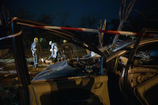 Ukrainian rescuers clear fallen trees near a destroyed car on a road in Kyiv on October 27, 2026, following a Russian missile strike. (Photo by Genya SAVILOV / AFP)