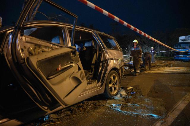 Ukrainian rescuers clear fallen trees near a destroyed car on a road in Kyiv on October 27, 2026, following a Russian missile strike. (Photo by Genya SAVILOV / AFP)