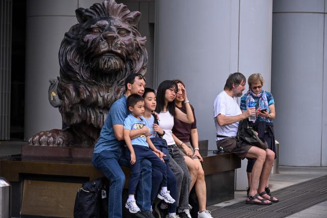 A family takes a photo with the bronze lion outside the HSBC bank headquarters in Hong Kong on October 27, 2026, ahead of the bank's third quarter results announcement. (Photo by Peter PARKS / AFP)