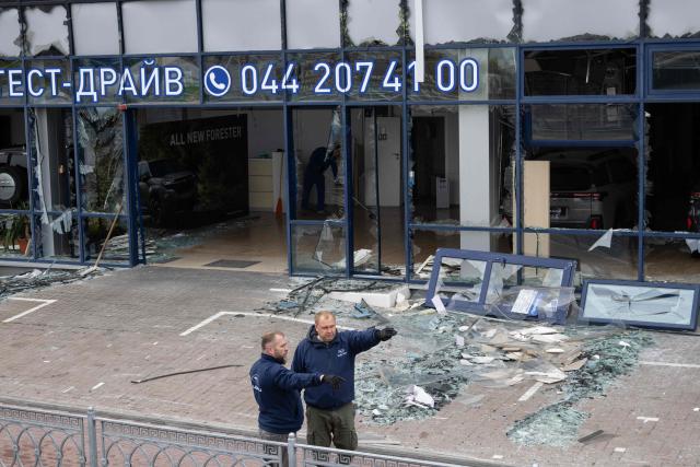 Workers stand next to a car dealership building damaged following an air attack in Kyiv on October 27, 2026, amid the Russian invasion of Ukraine. (Photo by Serhii Okunev / AFP)