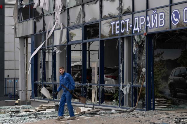 A worker walks next to a car dealership building damaged following an air attack in Kyiv on October 27, 2026, amid the Russian invasion of Ukraine. (Photo by Serhii Okunev / AFP)