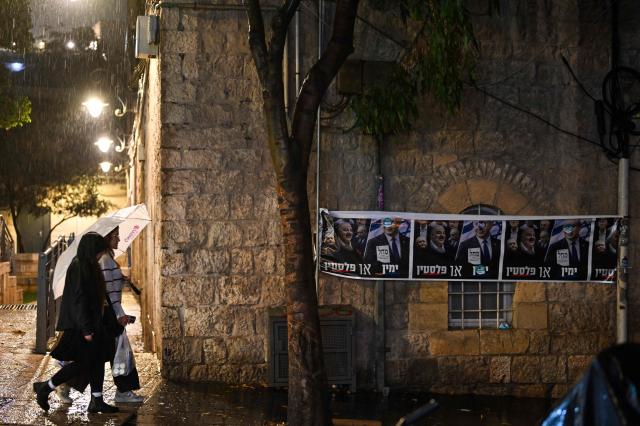 People walk with umbrellas in the rain outside a polling station in Jerusalem on October 27, 2026, on the day of Israel's legislative election. A deeply divided Israel headed to the polls for the first time since Hamas's October 7, 2023 attack, with voters delivering their verdict on veteran prime minister and the country's rightward drift. (Photo by Jewel SAMAD / AFP)