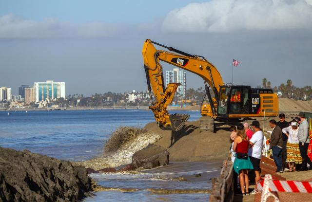 Residents watch as workers use an excavator to build a sand berm as preparations are underway for unusual high tides and coastal flooding in Long Beach, California, on October 27, 2026. The National Weather Service is warning of significant coastal flooding, expected during late-morning high tides for Southern California, through alerts until October 29. (Photo by Apu GOMES / AFP)