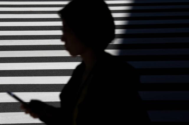 The silhouette of a woman using her phone along a street is pictured in Tokyo on October 28, 2026. (Photo by Yuichi YAMAZAKI / AFP)
