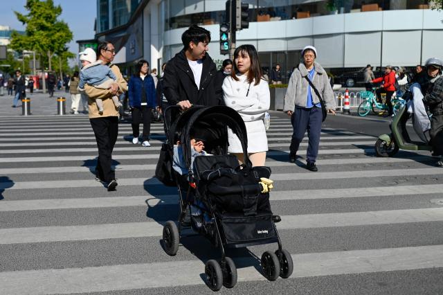 A man and a woman pushing a baby carriage cross a street in Beijing on October 28, 2026. (Photo by WANG Zhao / AFP)