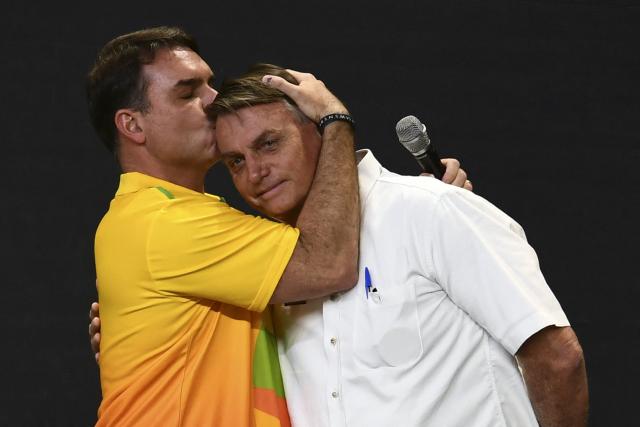 (FILES) (FILES) Brazil's senator Flavio Bolsonaro (L) kisses his father President Jair Bolsonaro during an event by the right-wing Liberal Party (PL), which he had officially joined last November in order to run in the October 2022 presidential election, at a convention centre in Brasilia, on March 27, 2022. Defeated right-wing presidential candidate Flavio Bolsonaro was on his way to Ecuador after fleeing Brazil, Argentina's government said on October 28, 2026. Bolsonaro entered Argentina the night before before boarding a flight to Ecuador, the country's National Directorate of Migration said on X. (Photo by EVARISTO SA / AFP)