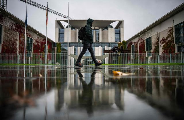 The chancellery and a pedestrian are reflected in the wet pavement as rain fell on Berlin on October 28, 2026. (Photo by John MACDOUGALL / AFP)