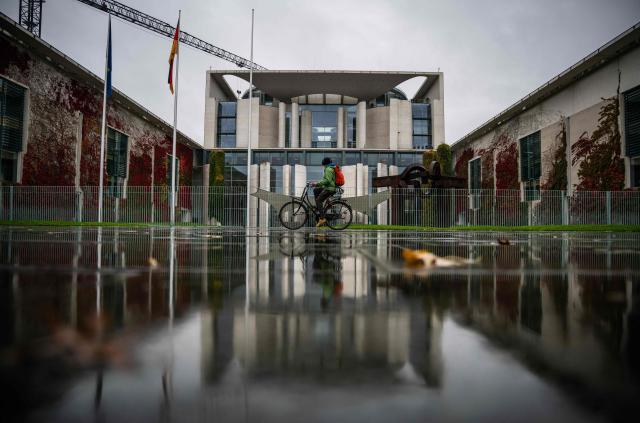 The chancellery and a cyclist are reflected in the wet pavement as rain fell on Berlin on October 28, 2026. (Photo by John MACDOUGALL / AFP)
