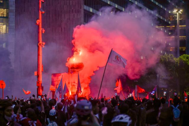 Protesters ignite a flare and wave flags during a demonstration against economic hardship, alleged government corruption, and toxic haze from wildfires, in Jakarta on October 28, 2026. (Photo by BAY ISMOYO / AFP)