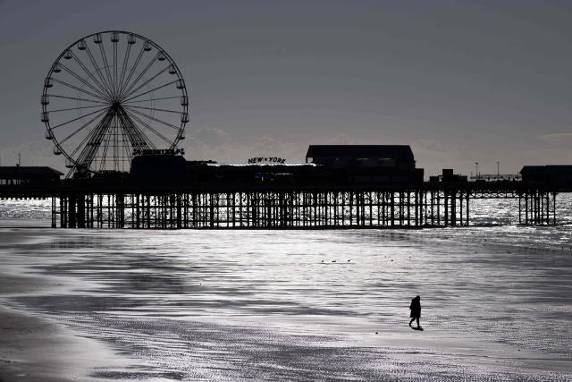 TOPSHOT - A person walks on the beach by the Central Pier in Blackpool, north-west England, on February 27, 2025. Blackpool, on the Irish Sea north of Liverpool and Manchester, embodies the rise and fall of the quintessential British seaside resort. But affordable air travel and holidays from the 1960s lured Britons overseas and knocked Blackpool off its perch. By 2008, it offered 40 percent fewer bed spaces than in 1987. (Photo by Oli SCARFF / AFP)