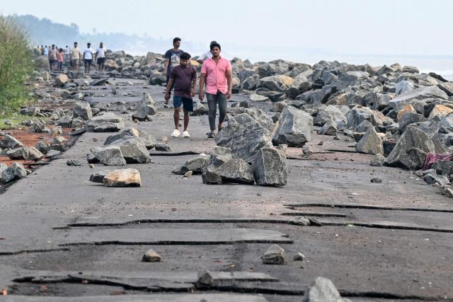 People walk along a coastal road past rocks moved by the storm surge after cyclone Arnab's landfall in Andhra Pradesh's Kakinada on October 29, 2026. Ferocious winds and torrential rain lashed India's southeastern coast after a cyclone made landfall on October 28, killing at least three people before the storm weakened, officials said. (Photo by Noah SEELAM / AFP)