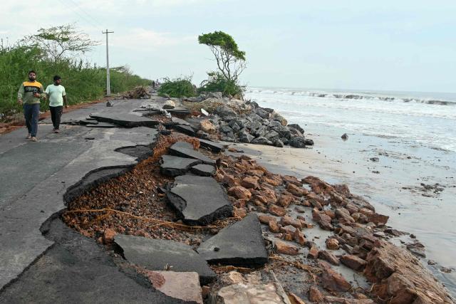 People walk along an eroded road on the coast after cyclone Arnab's landfall in Andhra Pradesh's Kakinada on October 29, 2026. Ferocious winds and torrential rain lashed India's southeastern coast after a cyclone made landfall on October 28, killing at least three people before the storm weakened, officials said. (Photo by NOAH SEELAM / AFP)