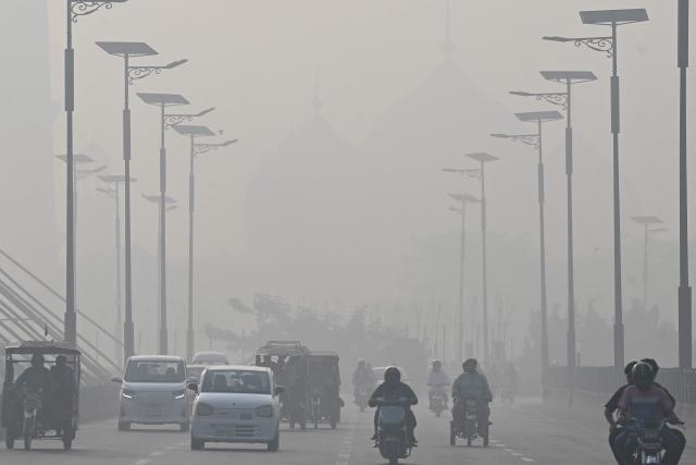 Commuters ride along a street amid smog in Lahore on October 29, 2026. (Photo by Arif ALI / AFP)