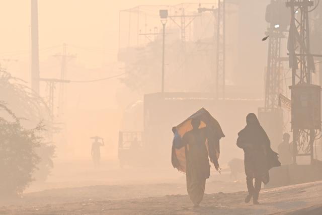 Women walk along a street amid smog in Lahore on October 29, 2026. (Photo by Arif ALI / AFP)