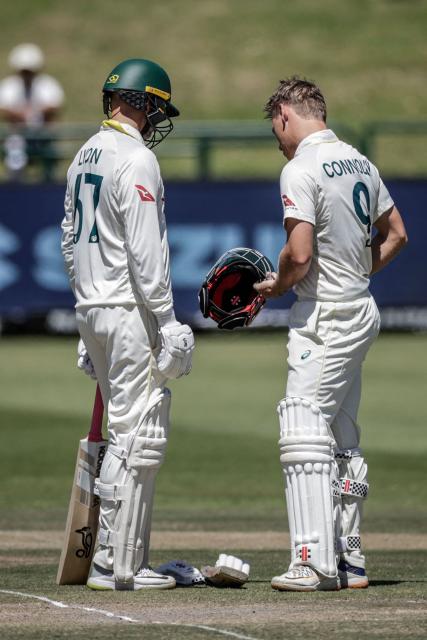 Australia's Cooper Connolly (R) checks his helmet next to Australia's Nathan Lyon after being hit by a ball on day three of the third Test match between South Africa and Australia at Newlands stadium in Cape Town on October 29, 2026. (Photo by Marco Longari / AFP)