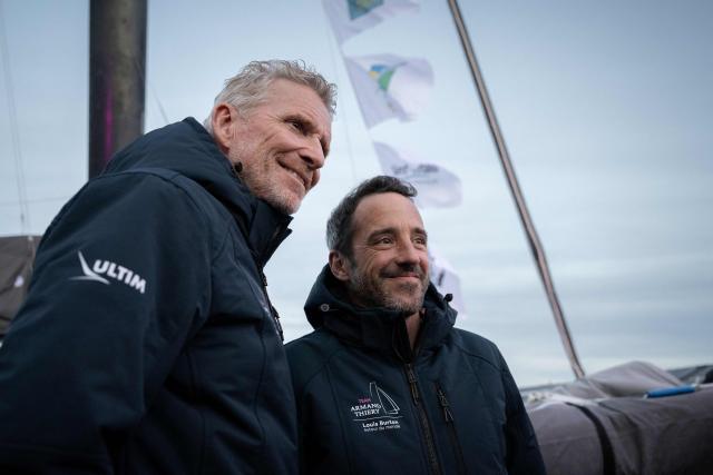 French television presenter Denis Brogniart (L) and French skipper Louis Burton pose for pictures prior to the inauguration of the Ultim multihull Armand Thiery, in the harbour of Saint-Malo northwestern France, on October 29, 2026 a few days prior to the start of the Route du Rhum solo sailing race from Saint-Malo, to Pointe-a-Pitre in the French overseas island of Guadeloupe. (Photo by Lou BENOIST / AFP)