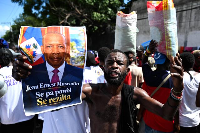 A supporter of Haitian public prosecutor and Government Commissioner Jean Ernest Muscadin shows a campaign poster with the slogan in Haitian Creole: "It’s not about words. It’s about results", as Muscadin arrives to an electoral office to register as a presidential candidate in Port-au-Prince, Haiti, on October 29, 2026. Haiti will hold the first round of presidential and legislative elections on July 18, 2027, the country's Provisional Electoral Council said on October 28, in what would mark the first polls in the crisis-stricken country in more than a decade. Elections are seen as a crucial step to stabilizing the government and tackling rampant crime in Haiti, which has been engulfed for years by gang warfare and political chaos. (Photo by Clarens SIFFROY / AFP)