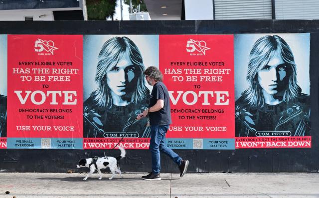 A man walks his dog past posters of the late Tom Petty reminding voters "every eligible voter has the right to be free to vote" in Hollywood, California on October 29, 2026. (Photo by Frederic J. BROWN / AFP)