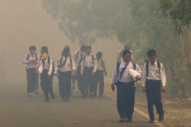 (FILES) Schoolchildren walk along a smoke-shrouded road in Tegal Arum, Banjarbaru, South Kalimantan, on October 20, 2026, as massive forest and land fires blanket the area in thick haze. Air pollution from smoke emitted by months of wildfires across Indonesia caused an estimated 3,560 deaths in the vast Southeast Asian archipelago in September alone, according to a scientific study. (Photo by MUDA SAGALA / AFP)