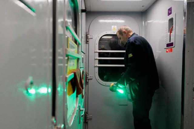 Mykola Kryvenko, 50 train attendant stands by the door with a flashlight while passengers are being evacuated from the train due to the threat of a Russian drone during the Kharkiv-Kyiv route on October 21, 2026, amid the Russian invasion of Ukraine. The approaching winter - many Ukrainians fear will be the harshest since the start of the war - is expected to make train travel more difficult still. Authorities are warning of possible disruptions to electricity, water and heating as Russia's attacks on energy infrastructure intensify. And as temperatures drop below freezing, evacuation will become more challenging. (Photo by Tetiana DZHAFAROVA / AFP)
