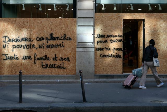 A pedestrian walks past a shop protected by wooden boards on which it is written (L) "Behind this boards, no power, no enemy", just a family and its job"  and (R) "One second to break, one life to build" a day ahead of new nationwide protests over the soaring cost of living and inequality in Paris on October 30, 2026. France has been rocked by widespread anger over the rising cost of living and inequality, with authorities warning of a "very high risk of public disorder" this weekend, after protests two weeks ago degenerated into some of the country's worst rioting in years. (Photo by Thomas SAMSON / AFP)