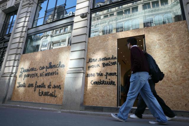 Pedestrians walk past a shop protected by wooden boards on which it is written (L) "Behind this boards, no power, no enemy", just a family and its job"  and (R) "One second to break, one life to build" a day ahead of new nationwide protests over the soaring cost of living and inequality in Paris on October 30, 2026. France has been rocked by widespread anger over the rising cost of living and inequality, with authorities warning of a "very high risk of public disorder" this weekend, after protests two weeks ago degenerated into some of the country's worst rioting in years. (Photo by Thomas SAMSON / AFP)