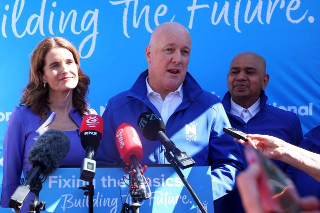(FILES) New Zealand Prime Minister Christopher Luxon (C) talks to the media alongside National Party deputy leader and Finance Minister Nicola Willis (L) during a general election campaign event in Tawa, a northernmost suburb of Wellington on September 29, 2026. Luxon told AFP on October 30, 2026, planned cuts to foreign aid would make sure the country spends less money on "nice-to-do" but frivolous projects abroad, and he vowed to push for new free trade deals from Brazil to Bangladesh if re-elected next week. (Photo by Ben STRANG / AFP)