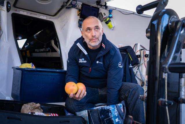 French skipper Fabrice Amedeo holds fruits as he restocks his Imoca monhull Fdj United - Ocean Calling in the harbour of Saint-Malo, northwestern France on October 30, 2026, a few days prior to the start of La Route du Rhum - Destination Guadeloup solo sailing race from Saint-Malo to Pointe-a-Pitre in the French overseas island of Guadeloupe. (Photo by Lou BENOIST / AFP)
