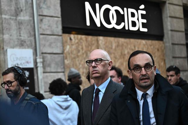 France's Economy, Finances and Industry Minister Roland Lescure (C) walks along with Bordeaux Mayor Thomas Cazenave (R) past the boarded-up ground-floor windows of a shop at the Saint-Catherine shopping district during a visit to the damaged stores during recent nationwide demonstrations, in Bordeaux, south-western France, on October 30, 2026. France has been rocked by widespread anger over the rising cost of living and inequality, with authorities warning of a "very high risk of public disorder" this weekend, after protests two weeks ago degenerated into some of the country's worst rioting in years. (Photo by Christophe ARCHAMBAULT / AFP)