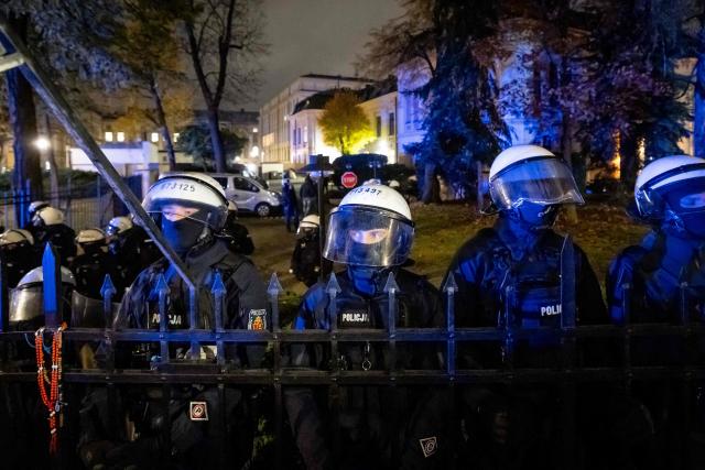 Police officers stand behind the fence with a rosary hanging on it as protesters gather outside the headquarters of Poland's Constitutional Court in Warsaw after police blocked access to the court building on 30 October, 2026 (Photo by Wojtek RADWANSKI / AFP)