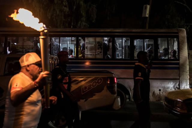 Passengers watch from a bus as a torchbearer carries the Youth Olympic Flame on the eve of the opening ceremony of the Youth Olympic Games in Dakar on October 30, 2026. Over the course of two weeks some 2,700 athletes aged 17 or younger are expected to compete across 25 sports, including Russians who are returning to the Games following a ban. Events ranging from athletics to beach wrestling, rugby sevens to breaking will be held across eight venues in three locations (Photo by PATRICK MEINHARDT / AFP)