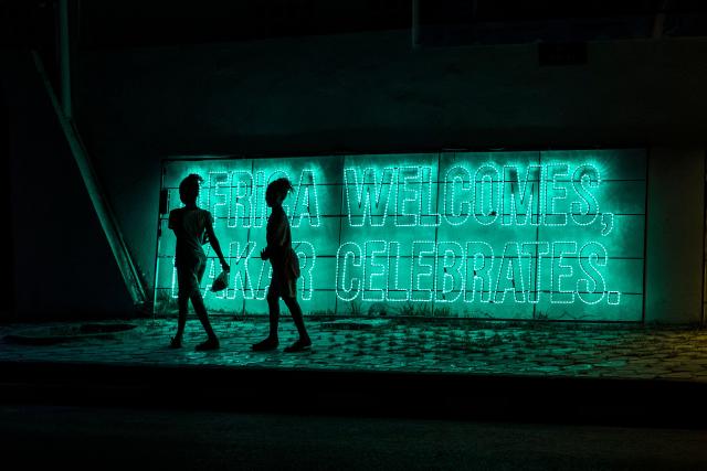 Girls walk past a sign that reads "Africa Welcomes, Dakar Celebrates" on the eve of the opening ceremony of the Youth Olympic Games in Dakar on October 30, 2026. Over the course of two weeks some 2,700 athletes aged 17 or younger are expected to compete across 25 sports, including Russians who are returning to the Games following a ban. Events ranging from athletics to beach wrestling, rugby sevens to breaking will be held across eight venues in three locations (Photo by PATRICK MEINHARDT / AFP)