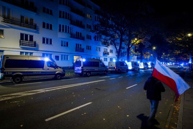 A man carrying a Polish national flag walks past a row of parked police trucks as protesters gather outside the headquarters of Poland's Constitutional Court in Warsaw after police blocked access to the building on October 30, 2026. Poland's President Karol Nawrocki called off a visit to Africa in mid-flight as riot police deployed around the country's constitutional court on October 30 following the suspension of its chief justice in a battle between the centrist government and the nationalist right. Dozens of police guarded the entrance to the court as followers of the opposition right-wing Law and Justice party (PiS) protested the ousting of constitutional court president Bogdan Swieczkowski. (Photo by Wojtek RADWANSKI / AFP)