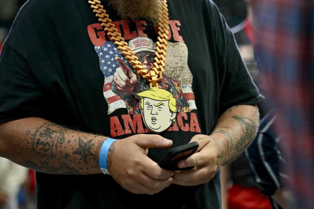 A supporter wears a T-shirt and a chain necklace with US President Donald Trump images at a midterm campaign rally at the Ocean Center in Daytona Beach, Florida on October 30, 2026. (Photo by Brendan SMIALOWSKI / AFP)