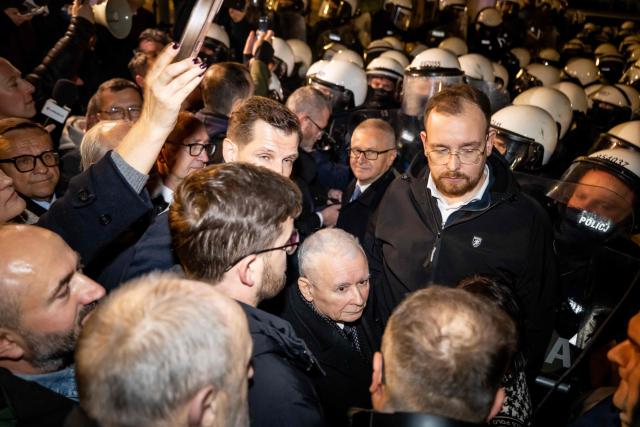 Poland's former Prime Minister and leader of the opposition Law and Justice (PiS) party, Jaroslaw Kaczynski (C), is seen between protesters gathered outside the headquarters of Poland's Constitutional Court in Warsaw after police blocked access to the building on October 30, 2026. Poland's President Karol Nawrocki called off a visit to Africa in mid-flight as riot police deployed around the country's constitutional court on October 30 following the suspension of its chief justice in a battle between the centrist government and the nationalist right. Dozens of police guarded the entrance to the court as followers of the opposition right-wing Law and Justice party (PiS) protested the ousting of constitutional court president Bogdan Swieczkowski. (Photo by Wojtek RADWANSKI / AFP)