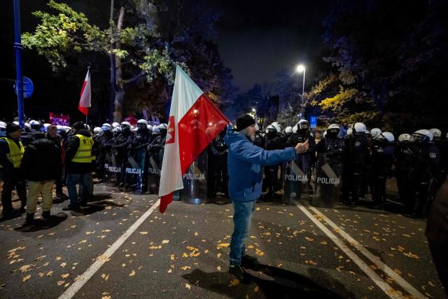 A man holding a Poland's national flag poses in front of a police cordon as protesters gather outside the headquarters of the Poland's Constitutional Court in Warsaw after police blocked access to the court building on October 31, 2026. Poland's President Karol Nawrocki called off a visit to Africa in mid-flight as riot police deployed around the country's constitutional court on October 30 following the suspension of its chief justice in a battle between the centrist government and the nationalist right. Dozens of police guarded the entrance to the court as followers of the opposition right-wing Law and Justice party (PiS) protested the ousting of constitutional court president Bogdan Swieczkowski. (Photo by Wojtek RADWANSKI / AFP)