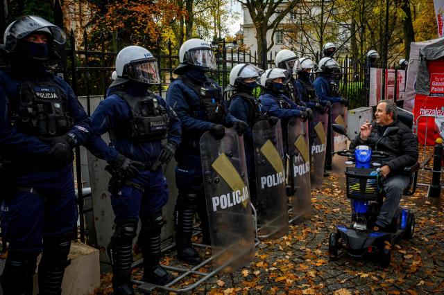 A protester in a wheelchair argues with police officers in riot gear as protesters gather outside the headquarters of Poland's Constitutional Court in Warsaw after police blocked access to the building on October 31, 2026. Poland's President Karol Nawrocki called off a visit to Africa in mid-flight as riot police deployed around the country's constitutional court on October 30 following the suspension of its chief justice in a battle between the centrist government and the nationalist right. Dozens of police guarded the entrance to the court as followers of the opposition right-wing Law and Justice party (PiS) protested the ousting of constitutional court president Bogdan Swieczkowski. (Photo by Mladen ANTONOV / AFP)